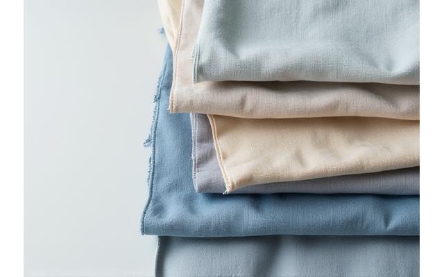 A stack of ethically sourced linen fabric swatches in various natural tones, highlighting texture.
